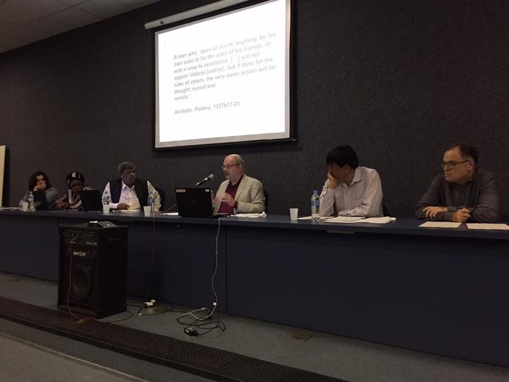 Image of speakers on a panel in front of a projection screen.